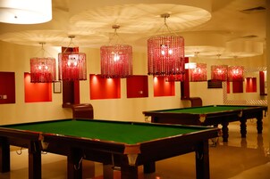 A pool table with a green felt surface, surrounded by red walls and multiple hanging red chandeliers.