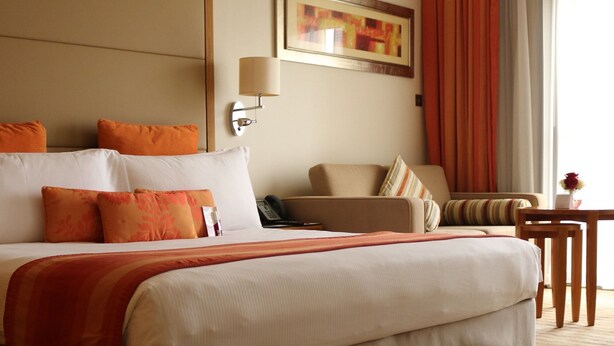 Una habitación de hotel con una cama grande, una silla, una mesita y un cuadro en la pared.