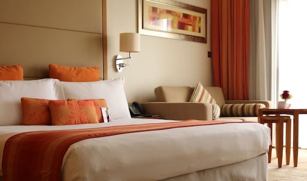 Una habitación de hotel con una cama grande, una silla, una mesita y un cuadro en la pared.