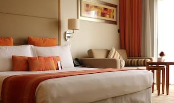 Una habitación de hotel con una cama grande, una silla, una mesita y un cuadro en la pared.