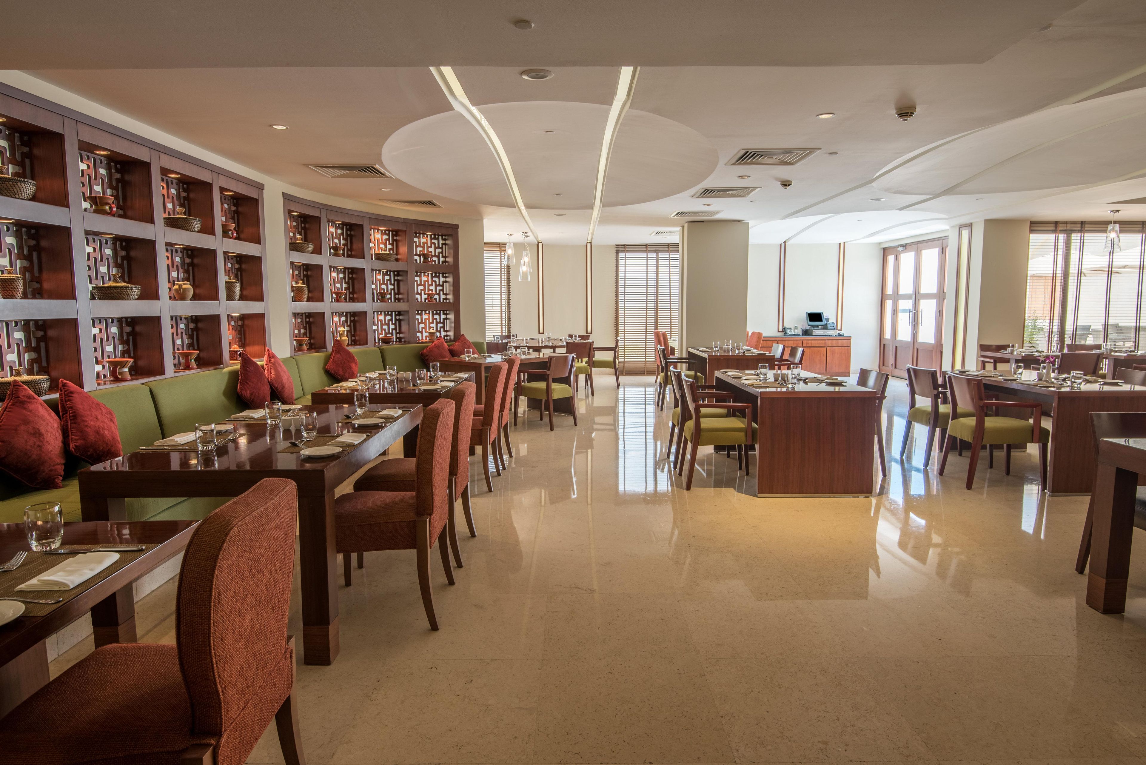 Un comedor amplio con varias mesas y sillas, una barra central y una gran estantería llena de libros.
