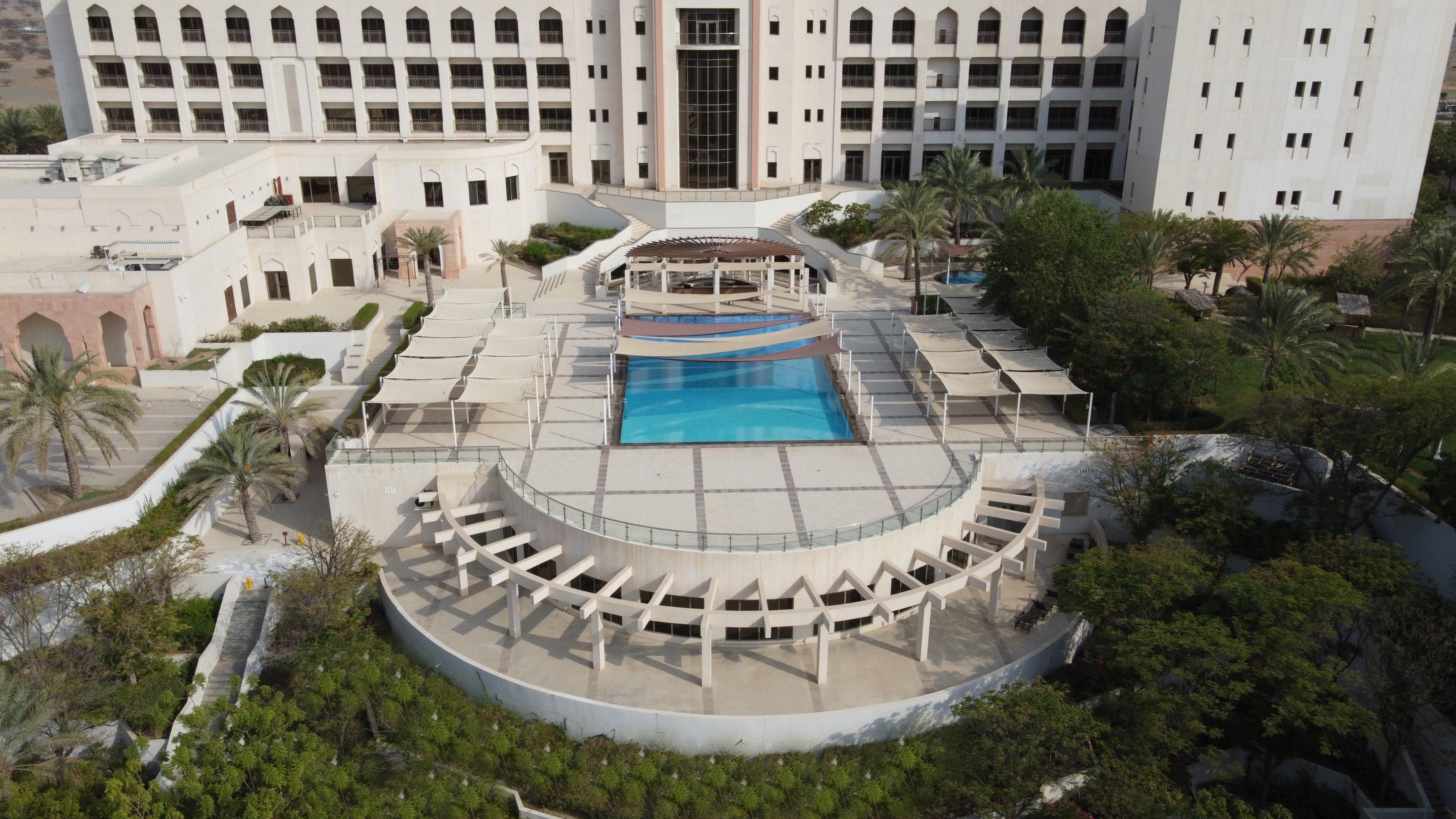 A hotel with a central swimming pool, a covered seating area, and a large building in the background.