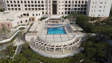 A hotel with a central swimming pool, a covered seating area, and a large building in the background.