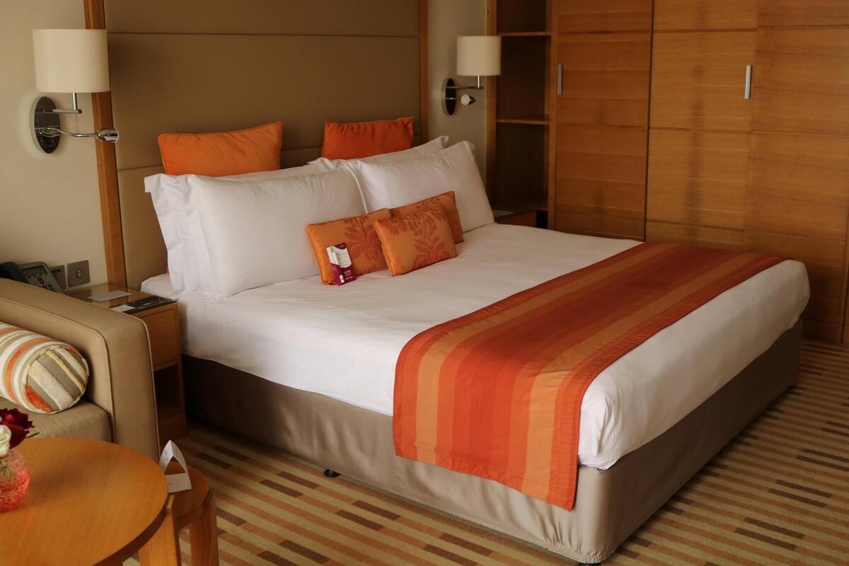 A hotel room with a large bed, two bedside tables, a nightstand, a wooden wardrobe, and a small round table with a vase.