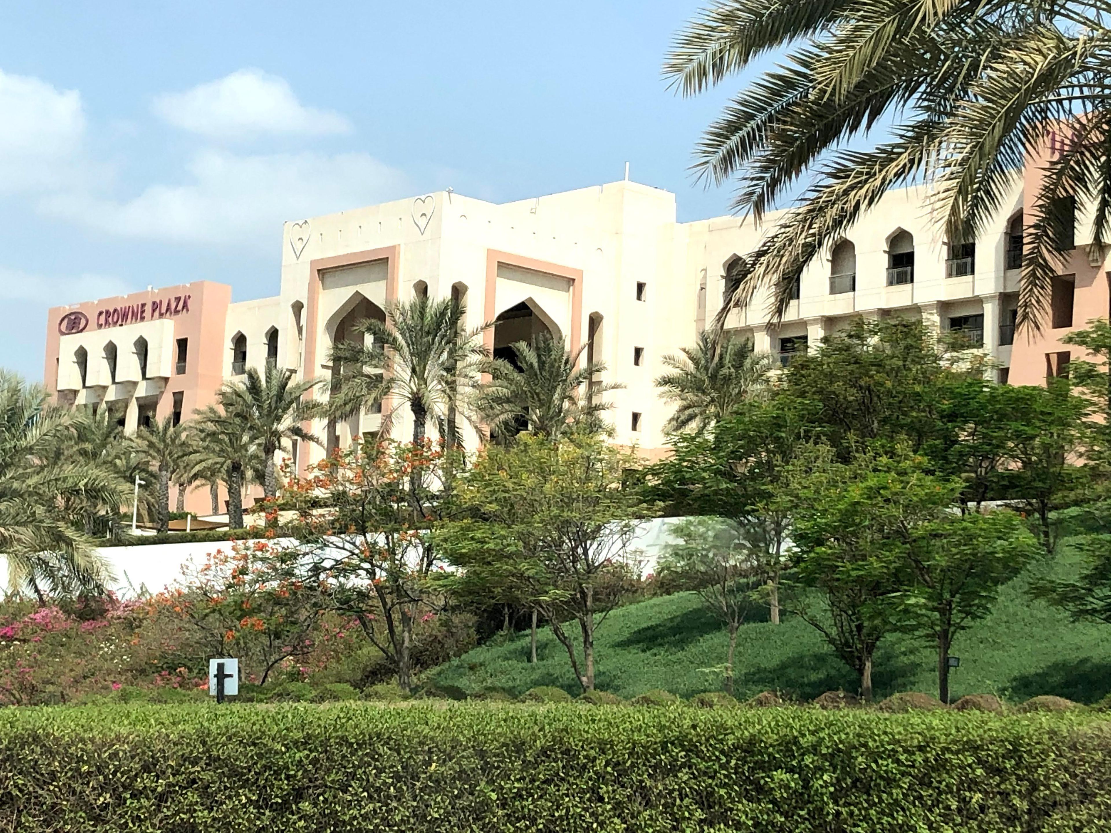 A building with a sign reading 'Crowne Plaza' surrounded by palm trees and greenery.