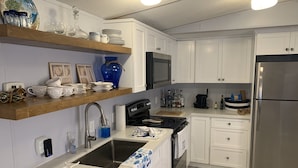 A modern kitchen with white cabinets, a stainless steel refrigerator, a microwave, and a dishwasher. There are shelves with decorative items and a sink with a faucet.