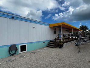 A building with a blue and white exterior, a yellow awning, and a gravel ground. - Family Fishing Shack Tavernier Key (Tavernier)
