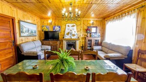 A cozy wooden cabin interior with a dining table, chairs, sofas, a fireplace, and a television. - Las Olivas Sayalonga by Ruralidays (Málaga)