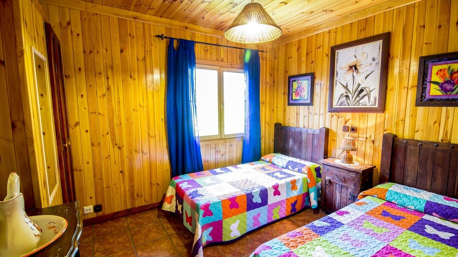 Une pièce en bois avec deux lits, une fenêtre ornée de rideaux bleus et une tête de lit en bois.