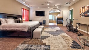 Una camera da letto con un letto, una TV, una bicicletta e un angolo cottura sullo sfondo.