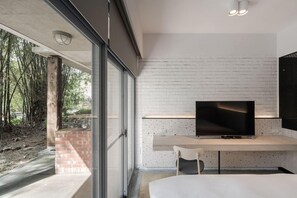 A modern bedroom with a large bed, a TV on a wooden stand, and a glass door leading to a balcony with a view of trees. - The Moment Hotel Yilan by Lakeshore (Wujie)