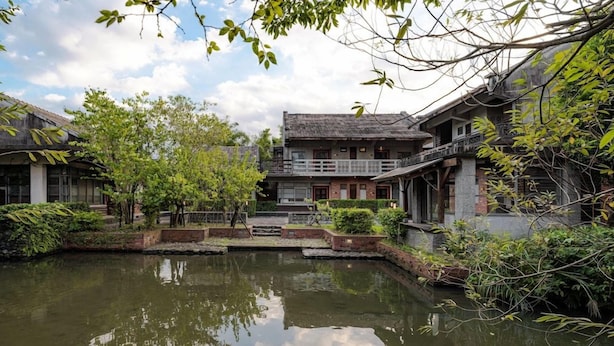 Un patio tradicional con un estanque, rodeado de edificios con balcones y un puente de madera.