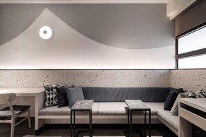 A modern interior with a curved ceiling, a seating area with a sofa and two tables, and a kitchenette with a window. - The Moment Hotel Yilan by Lakeshore (Wujie)