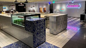 Vestíbulo de hotel con mostrador de recepción, baldosas estampadas y un letrero de neón.