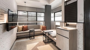 Una cocina moderna con estufa integrada, una zona de estar con sofá y una mesa pequeña, y un ventanal que proporciona luz natural.