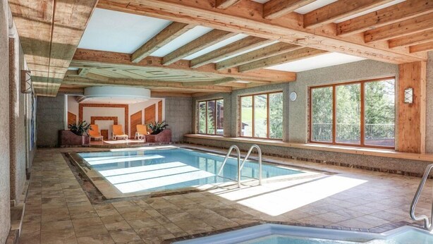 Piscina interna com teto de madeira e grandes janelas.