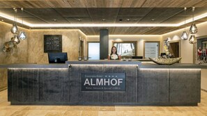 A hotel reception area with a modern design, featuring a reception desk labeled "Panorama Hotel ALMHOF" and a sign indicating "Nature, Wellness & Spa on 1600 m". - Almhof Hotel (Galtur)