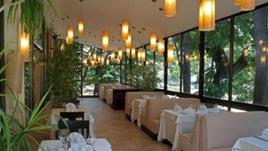 Un restaurant avec des tables dressées, de grandes fenêtres et des luminaires suspendus.