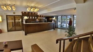Un espace d’accueil comprenant un comptoir de réception, deux réceptionnistes et un escalier menant à l’étage supérieur.