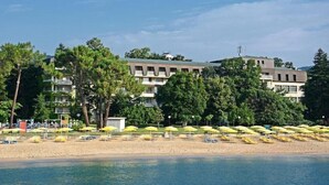 Un hôtel situé en bord de mer, avec plusieurs étages, une plage de sable et de nombreux parasols jaunes.