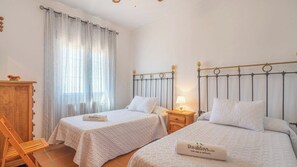 Une chambre d’hôtel avec deux lits, une chaise en bois, une table de chevet avec une lampe et une fenêtre avec des rideaux.