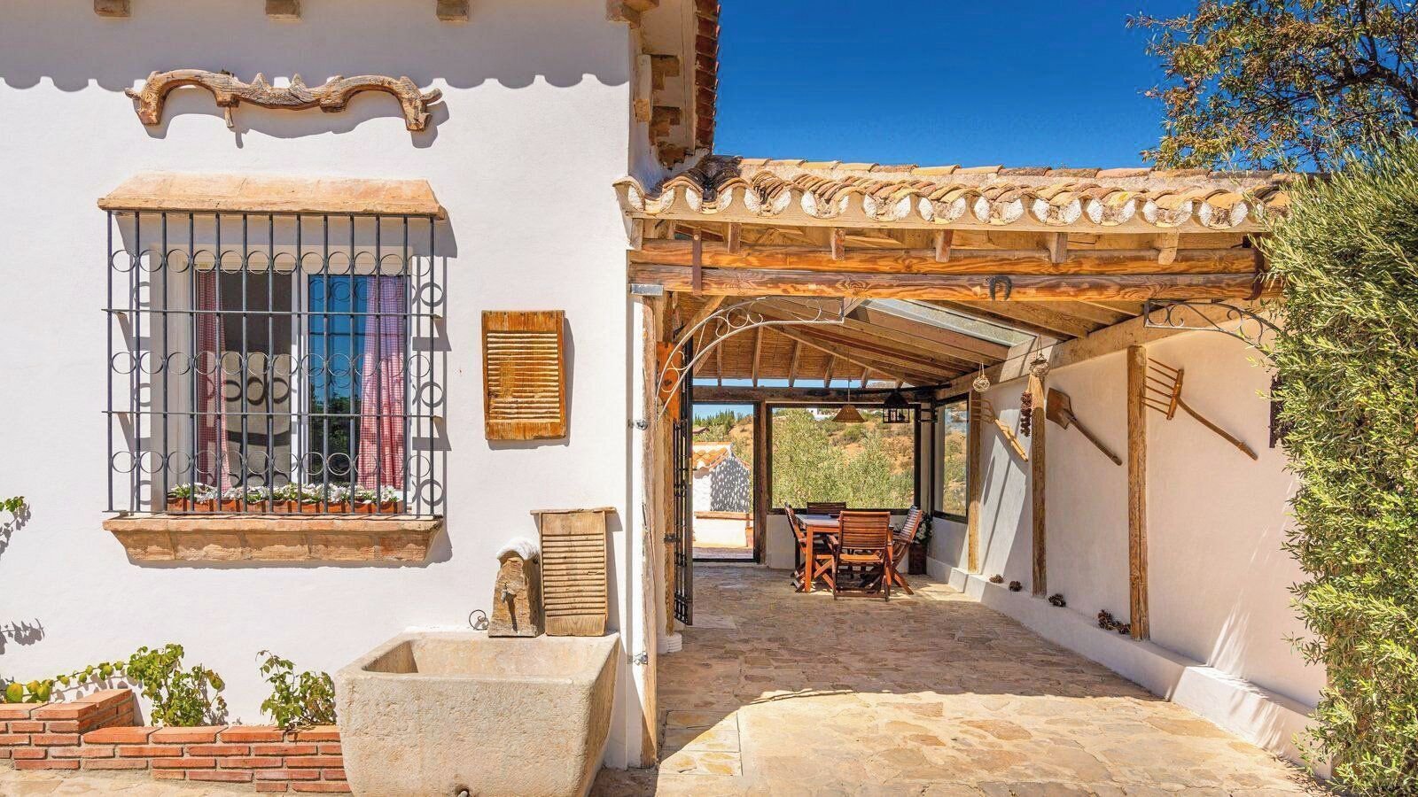 Ein traditionelles Gebäude mit überdachter Terrasse, einem Fenster mit Gitterstäben und einem Tisch mit Stühlen.