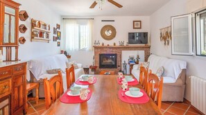 Un coin repas avec une table en bois dressée pour quatre personnes, entourée de chaises, d’une cheminée et d’un téléviseur fixé au mur.