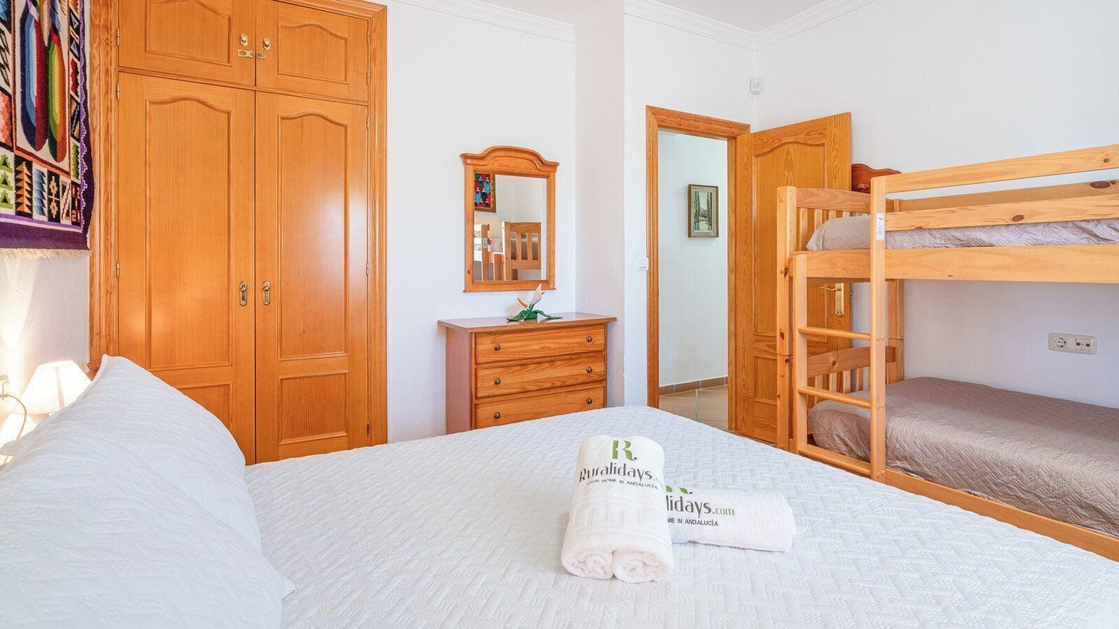 A hotel room with a bed, a wooden wardrobe, a dresser, a mirror, and a bunk bed.