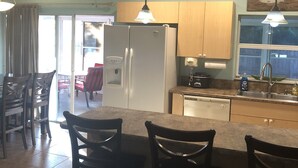 Una cocina con refrigerador, pileta y comedor con sillas.