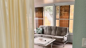 Una habitación con sofá, mesa de centro y ventana que da a una valla de madera y árboles.