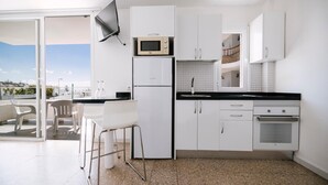 A modern kitchen with white cabinets, a microwave, a refrigerator, and a built-in oven. There is a dining area with white chairs and a small table. - Apartamentos Livvo Tarahal (San Bartolomé de Tirajana)
