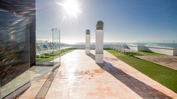 A sunlit outdoor area with a pathway, white columns, and rows of sun loungers. - Apartamentos Livvo Tarahal (San Bartolomé de Tirajana)