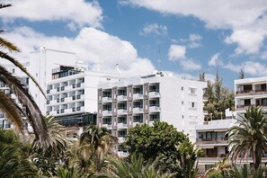 Un hotel de varios pisos con balcones, rodeado de palmeras bajo un cielo parcialmente nublado.