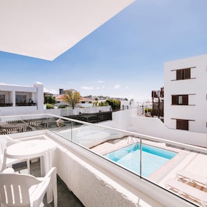 Un espace piscine sur le toit, doté d’une balustrade en verre, d’une piscine et de chaises longues blanches.