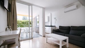 Una sala moderna con un sofá, una mesa de centro y un comedor con sillas y una mesa. Hay una puerta corrediza de vidrio que da a un patio exterior.