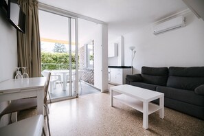 A modern living room with a sofa, a coffee table, and a dining area with chairs and a table. There is a sliding glass door leading to an outdoor patio. - Apartamentos Livvo Tarahal (San Bartolomé de Tirajana)