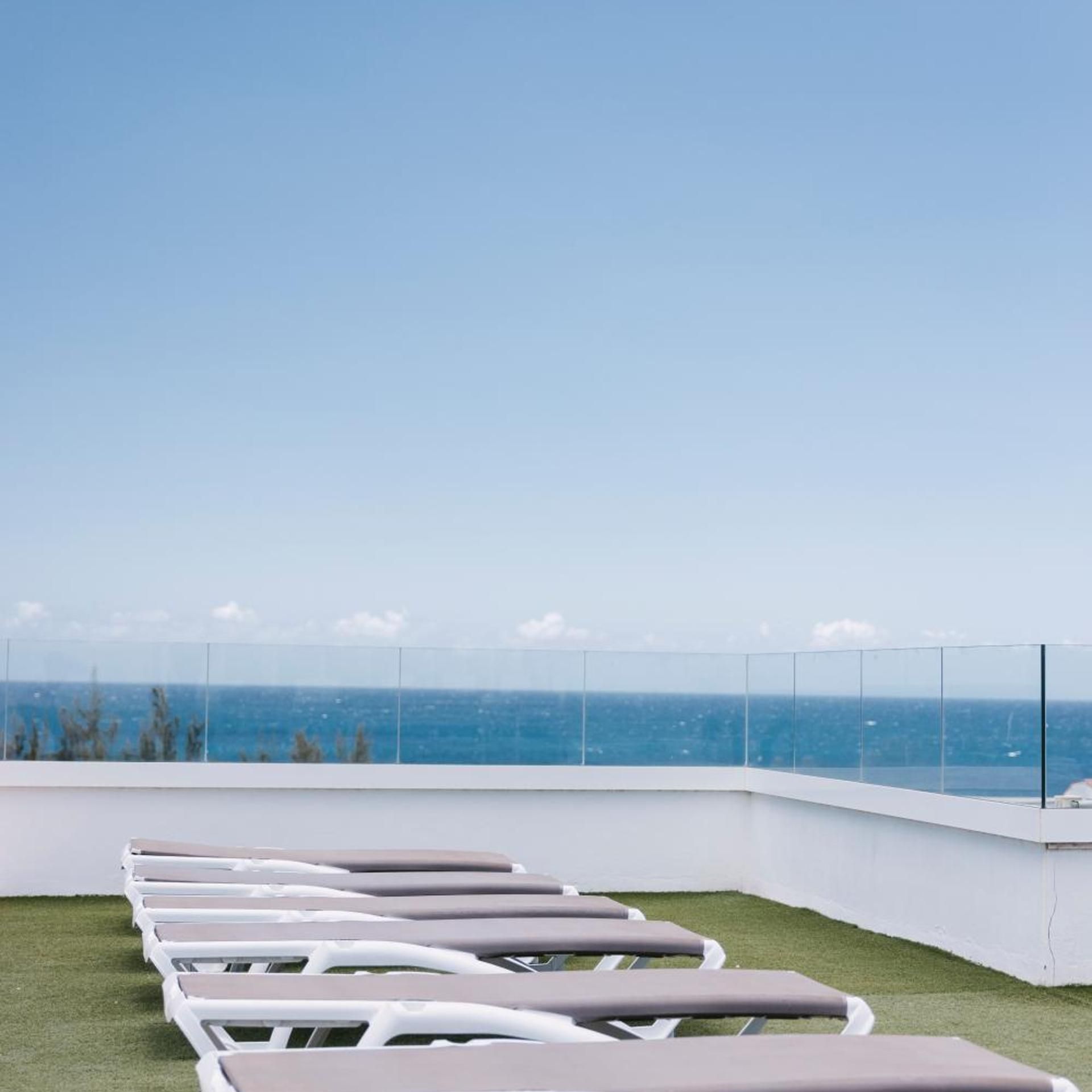A row of sun loungers on a rooftop with a clear view of the ocean.