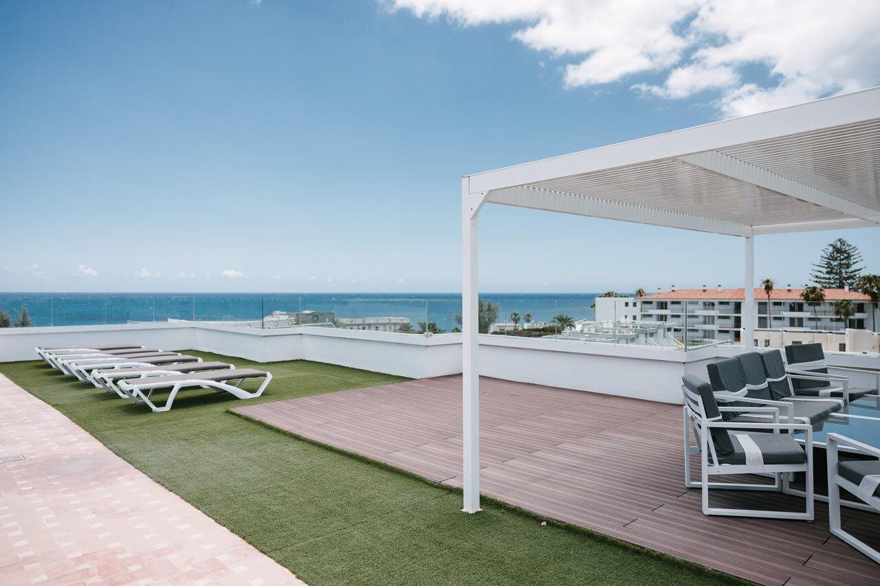 A rooftop terrace with lounge chairs and a table, overlooking a coastal cityscape.