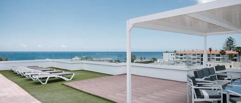 A rooftop terrace with lounge chairs and a table, overlooking a coastal cityscape.