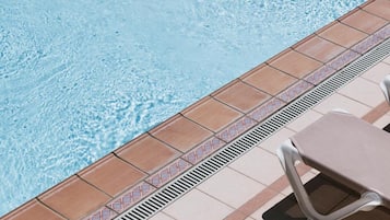 Una piscina con agua cristalina, borde de azulejos y dos tumbonas.