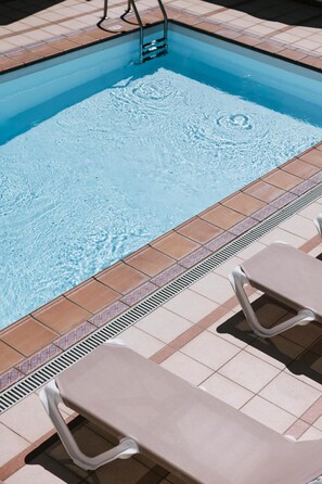 Una piscina con agua cristalina, borde de azulejos y dos tumbonas.