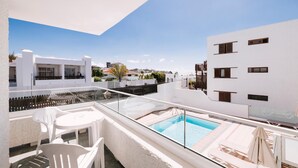 A rooftop pool area with a glass balustrade, white chairs, and a clear view of the surrounding buildings. - Apartamentos Livvo Tarahal (San Bartolomé de Tirajana)