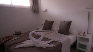 Una habitación de hotel con cama, mesita de noche, espejo y ventana con cortinas.