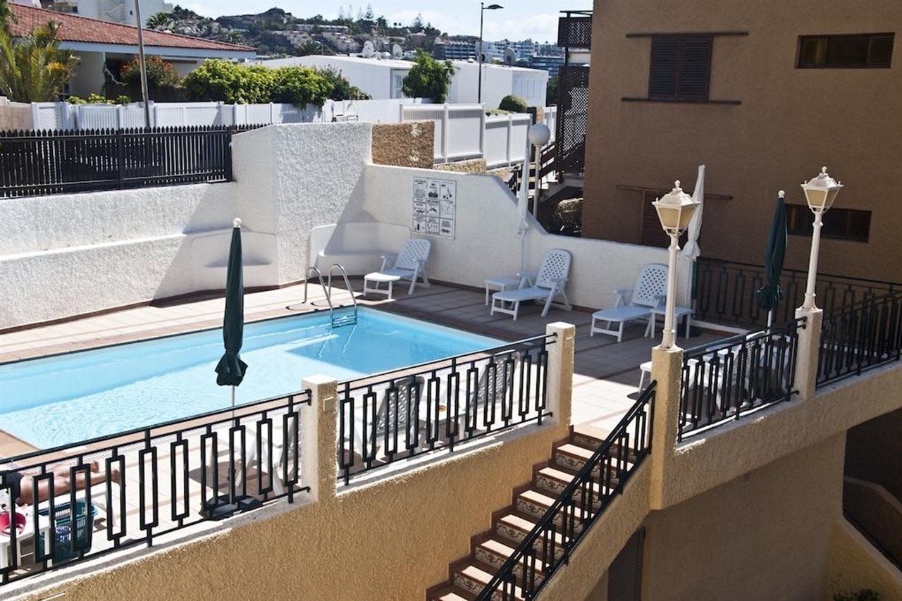 Una piscina en la azotea con sillas de descanso blancas y una escalera que conduce a un nivel superior.