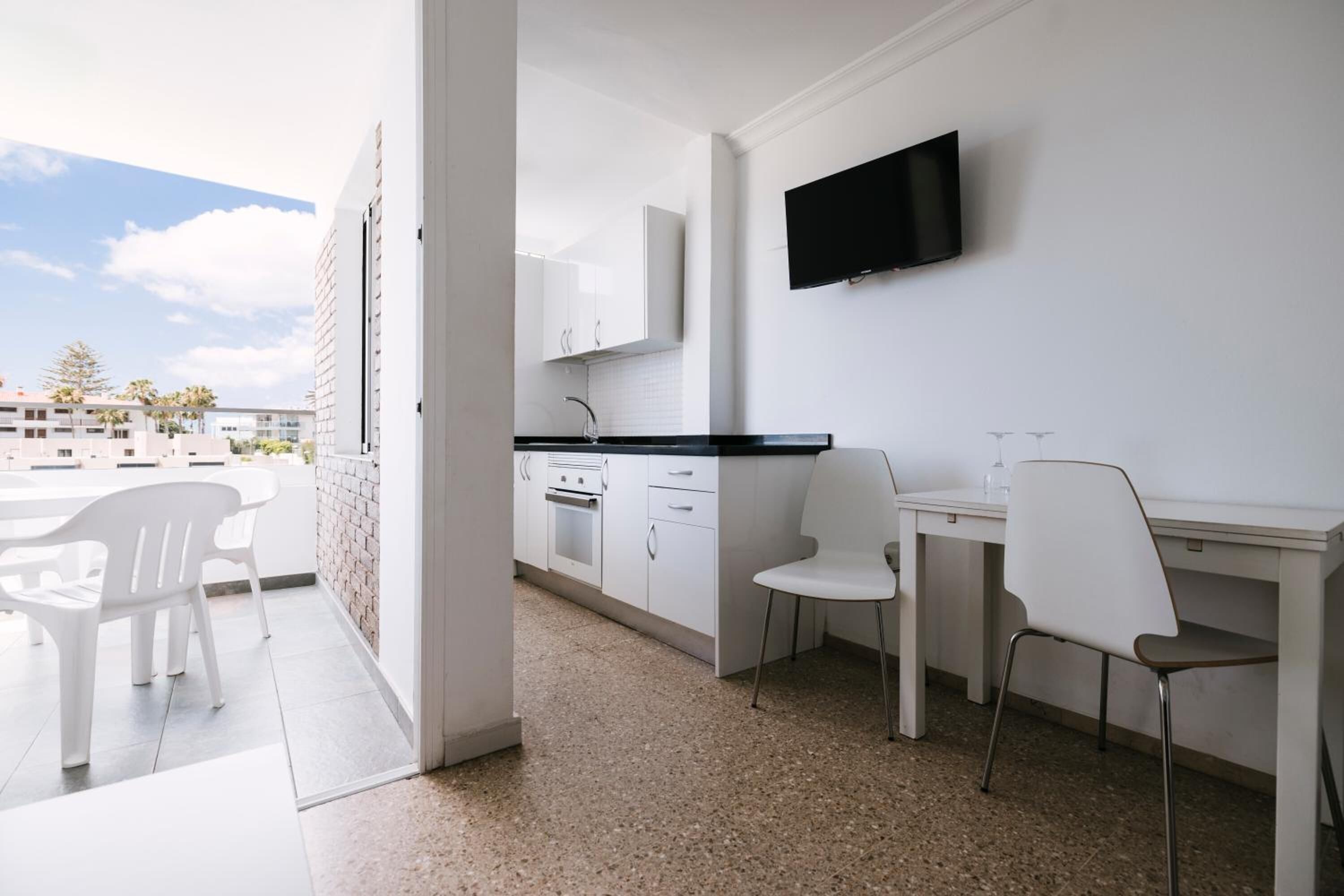 A modern kitchen with white cabinets, a black countertop, and a flat-screen TV mounted above the counter.