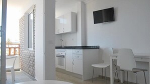 Una cocina moderna con armarios blancos, encimera negra y televisor de pantalla plana montado en la pared.