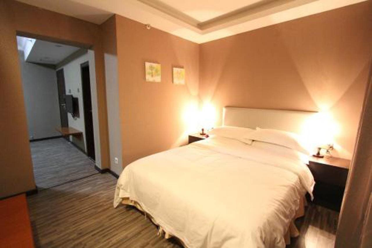 A hotel room with a large bed, two bedside tables, and a nightstand. There is a door leading to another room and a hallway.