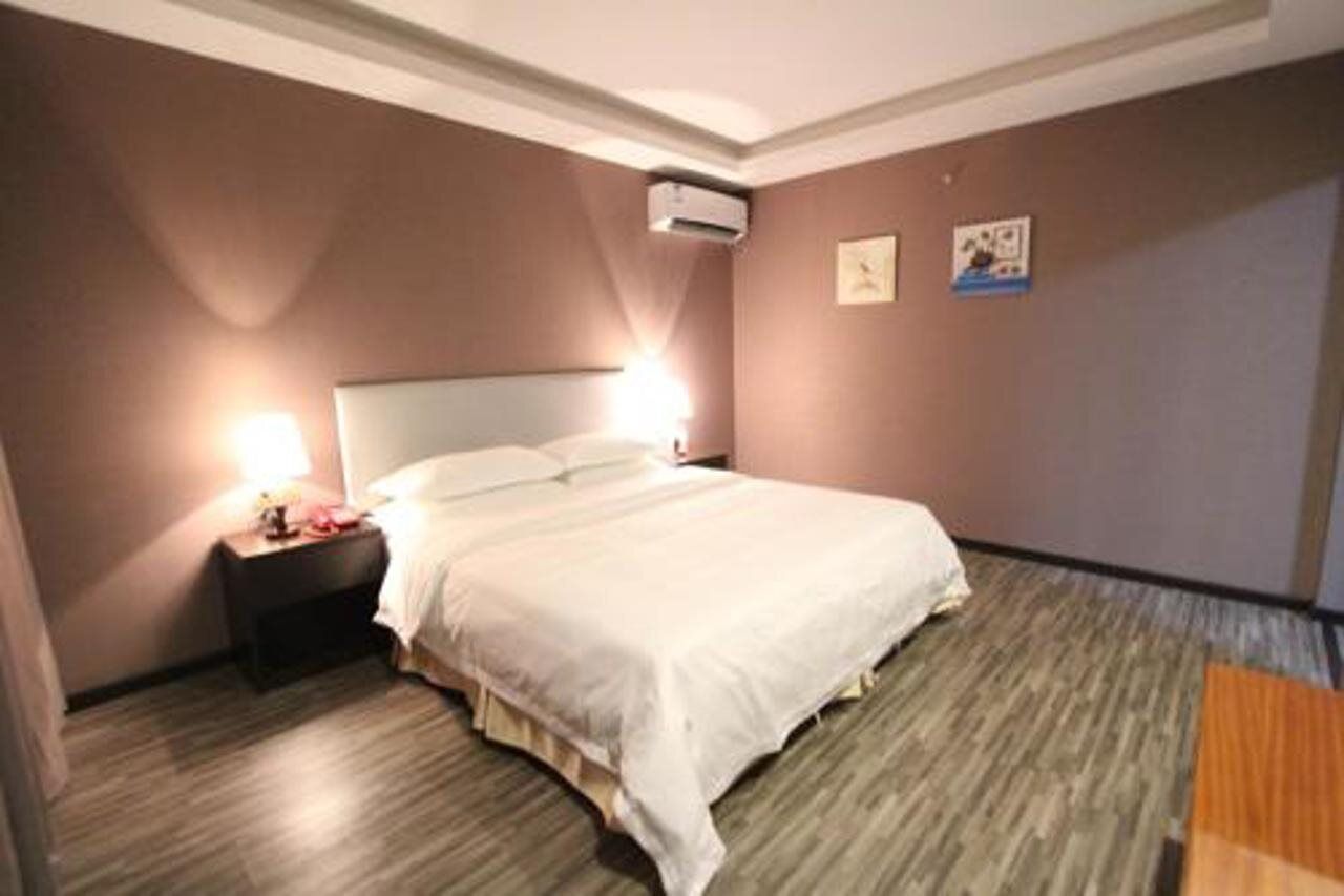 A hotel room with a bed, nightstand, and wall-mounted air conditioning unit.