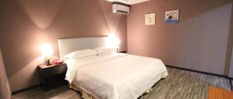 A hotel room with a bed, nightstand, and wall-mounted air conditioning unit.