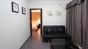 A room with a black sofa, a small table, and a bed in the background. There are two framed pictures on the wall. - J.S Fashion Hotel (Zhuhai)